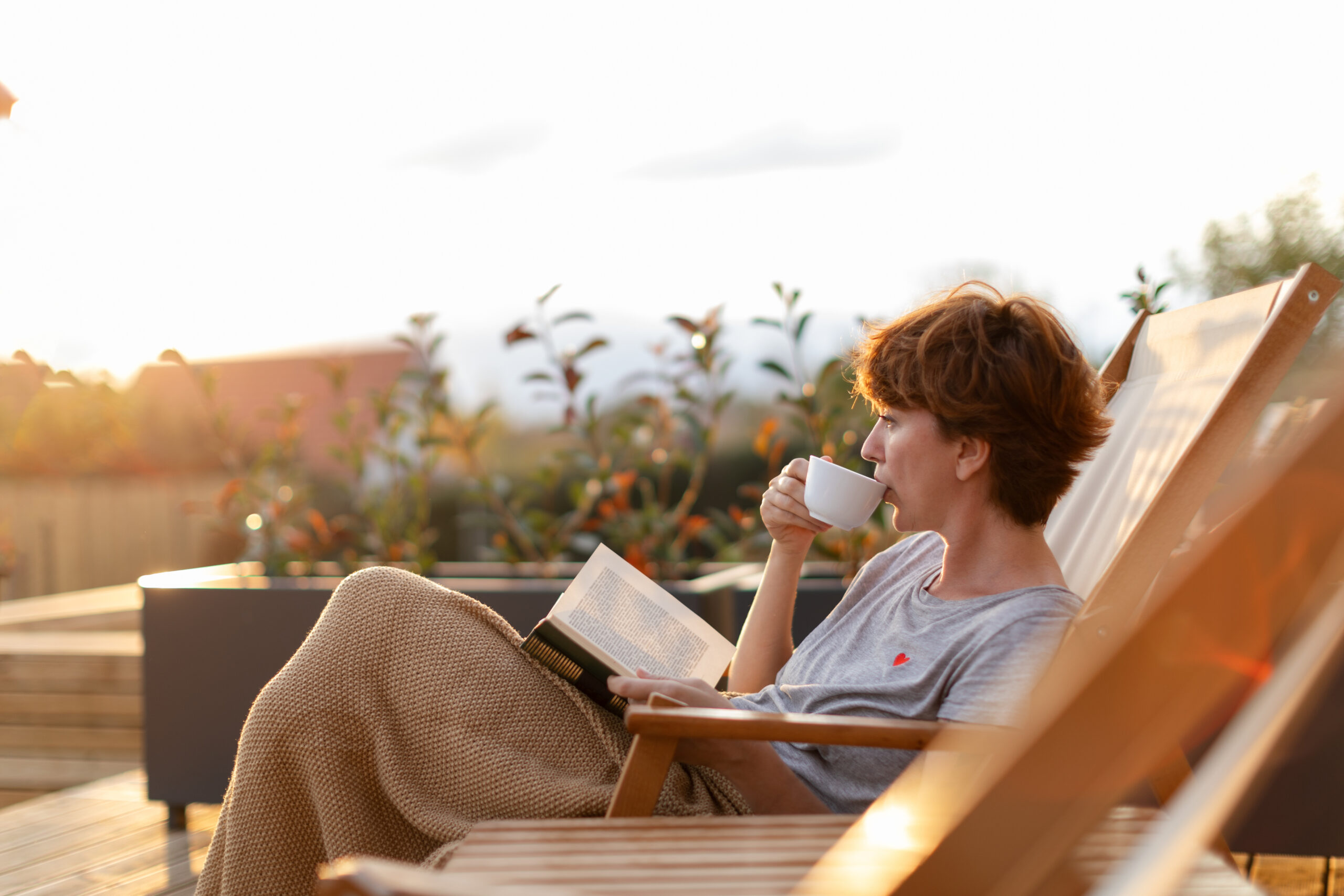 Person relaxing with book and coffee outdoors.