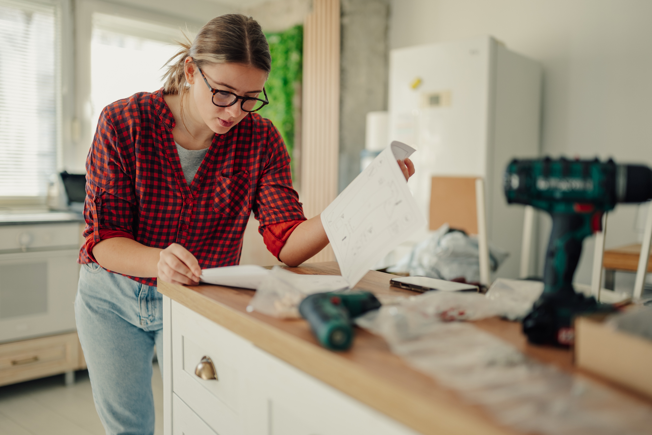 Young woman reading assembly instructions on paper, doing home improvement project, standing at a kitchen countertop with tools