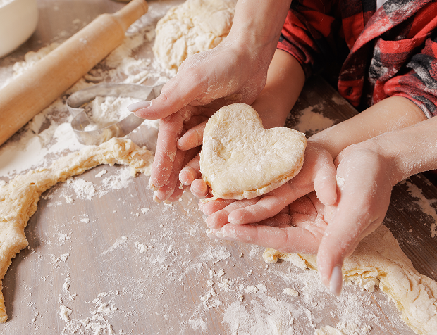 Hands shaping heart-shaped dough piece.