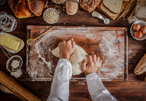 Baker kneading dough on wooden table.